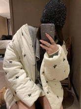 Person wearing a white puffer jacket with black patterns indoors.